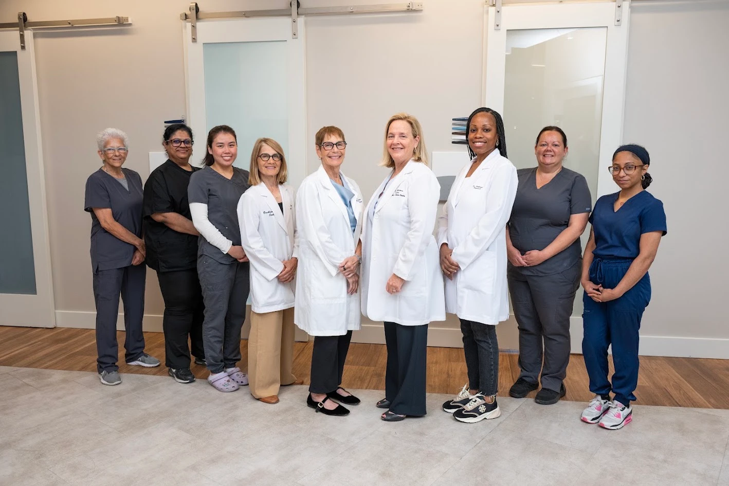 Nine women, some in lab coats and some in scrubs, stand smiling in a line.