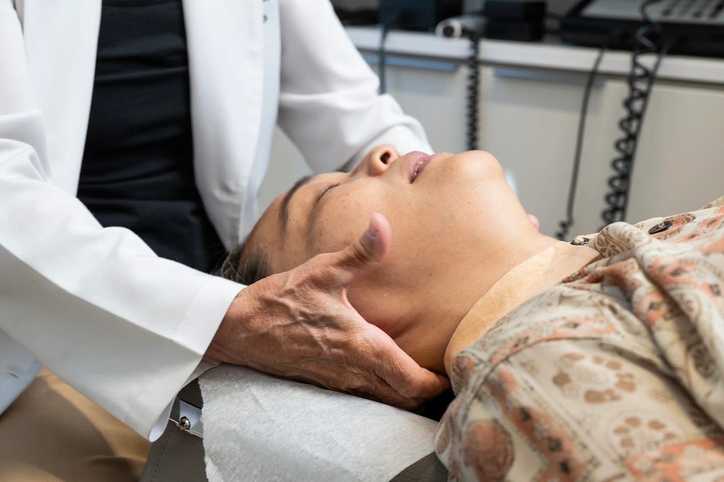 A practitioner in a white lab coat performs a neck adjustment on a patient lying down.