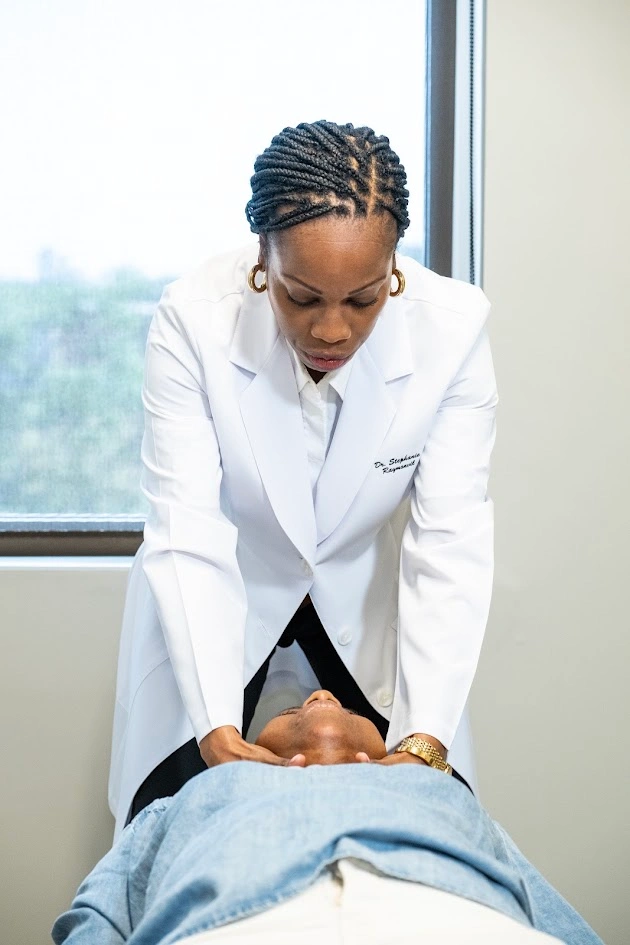 A female doctor in a white lab coat gently examining a patient's neck.