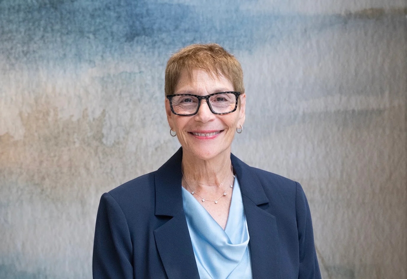 Headshot of a smiling woman with short brown hair, glasses, and a blue blazer.