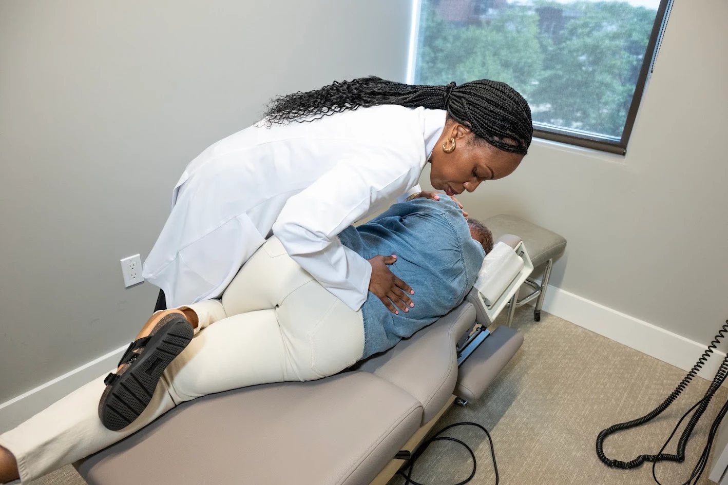 A practitioner in a white coat adjusts a patient lying on their side on an examination table.