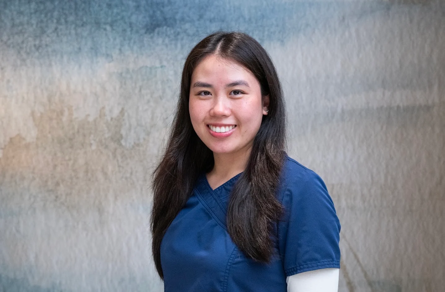 Headshot of Sabrina with long dark hair, wearing a blue scrub top.